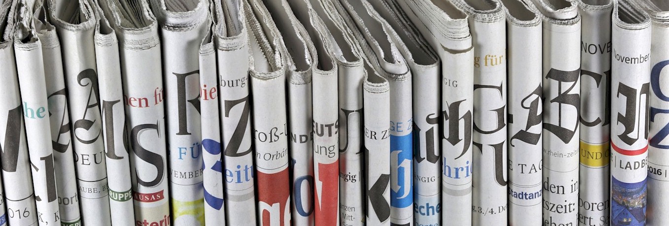 Das Foto zeigt viele aufrecht nebeneinander stehende Zeitungen. Der Batrachter blickt auf die Rücken der zusammengefalteten Zeitungen.
