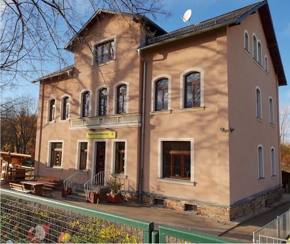 Das Bild zeigt das Gebäude des Vereins am Standort Lugau. Es ist ein rosafarbenes, zweistöckiges Gebäude mit Rundbogenfenstern im Obergeschoß